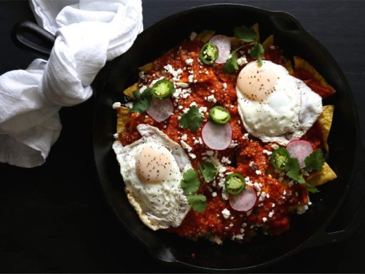 CHILAQUILES <br/><br/>INGREDIENTES <br/>450 gramos de tomates, sin semillas y cortados en trozos grandes /1 jalapeño, sin semillas, cortado en trozos grandes / 1 cebolla amarilla pequeña, finamente picada /Aceite de canola / Sal / 1/4 taza de hojas de cilantro/ 5 cucharadas de jugo de limón fresco/ 3 cucharadas de crema agria o mantequilla crema / 12 tortillas de maíz, cortadas en tiras gruesas o triángulos y fritas al gusto/ 1/4 taza de queso feta desmenuzado / 4 huevos<br/><br/>PREPARACIÓN<br/>1/ Calienta el horno a 220 °C. 2/Prepara una bandeja para hornear con papel encerado. Coloca ahí los tomates, jalapeño y cebolla, rocía con una cucharada de aceite de canola y 1/2 cucharadita de sal. Asa los vegetales, moviéndolos de vez en cuando, alrededor de 20 minutos. 3/ Licúa los vegetales rostizados y agrega el cilantro y 3 cucharadas de jugo de limón. Procesa hasta conseguir una consistencia homogénea. Salpimenta. 4/ En un bol pequeño, mezcla la crema agria y las otros 2 cucharadas de jugo de limón. Sazona. Reserva. 5/ En una cacerola de mediana profundidad, coloca la salsa de tomates y hierve. 6/ Disminuye el fuego, agrega las tortillas fritas y cocina revolviendo de vez en cuando, aproximadamente cinco minutos 7/ Vierte encima y con mucho cuidado cada huevo para que se cocinen en la salsa, unos tres minutos más. No cocines demasiado para que las tortillas queden suaves. 8/ Divide los chilaquiles en cuatro platos y coloca encima de cada uno un cuarto de la crema agria, queso feta y cilantro picado.<br/>