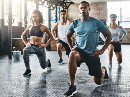 Shot of a group of young people doing lunges together during their workout in a gym Shot of a group of young people doing lunges together during their workout in a gym