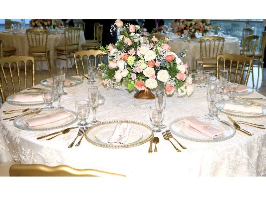 Las mesas circulares fueron adornadas con un masivo arreglo estilo bouquet de rosas ivory y rosadas, nardos, hortensias y baby breath y en las bases la servilleta tenía una cruz como recuerdo de la celebración.