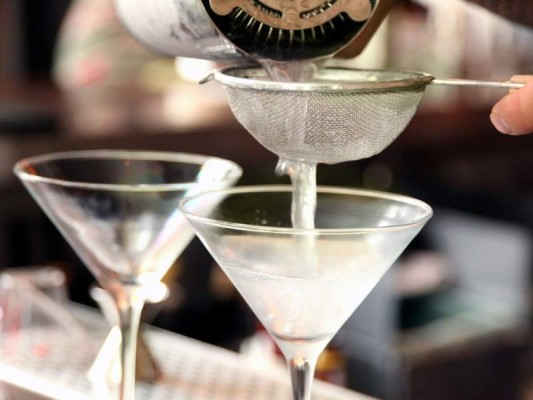 a bartender pouring martinis into chilled glasses through a small wire mesh strainer.