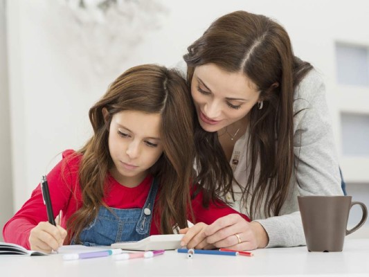 Happy Young Mother Helping Her Daughter While Studying At Home