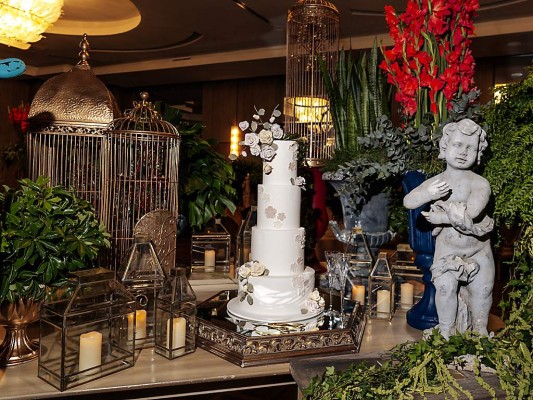Lámparas estilo antiguo, estatuas y grandes macetas adornaron la mesa del pastel de bodas de 4 niveles elaborado por los expertos de Signature Cake.