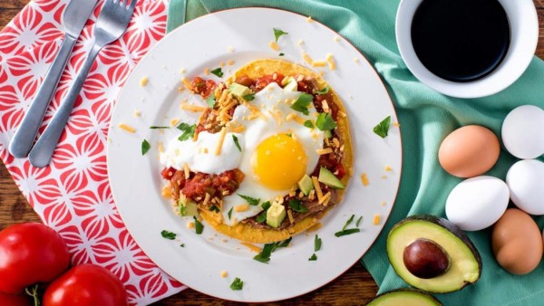 HUEVOS RANCHEROS<br/><br/>INGREDIENTES <br/>4 tazas espinaca cortada/ 4 huevos / 1/4 taza cilantro fresco picado / 1/2 taza queso cheddar rallado/ 1 aguacate pequeño en cubos/ 4 tortillas de maíz tostadas o fritas/ 4 cucharadas de frijoles molidos o fritos /PARA LA SALSA 1 cebolla blanca pequeña finamente picada/ 1 cucharada mantequilla / 2 dientes de ajo finamente picado / 2 pimientos rojos picados sin semilla/ 2 hojas laurel / 1 cucharadita paprika / 1 pizca pimienta cayena / 5 tazas tomate maduro picado / una pizca sal gruesa<br/><br/>PREPARACIÓN <br/>1/ Primero prepara la salsa de tomate. En una sartén ancha saltea la cebolla con la mantequilla hasta que esté traslúcida.2/ Añade el ajo, pimiento, hojas de laurel y demás especies. Cocina a fuego medio por aproximadamente 2 minutos. 3/ Añade el tomate en cubos y un cuarto de taza de agua, salpimenta. 4/ Deja que se cocinen los ingredientes hasta que obtenga una textura espesa, de 10 a 15 minutos. 5/ Fríe o tuesta las tortillas, reserva calientes. 6/ Fríe los huevos uno a uno.7/ Para el Montaje: Unta cada tortilla con una cucharada de frijoles calientes, baña con salsa de tomate, coloca encima un huevo estrellado y un poco de aguacate, rocía con el queso.<br/>