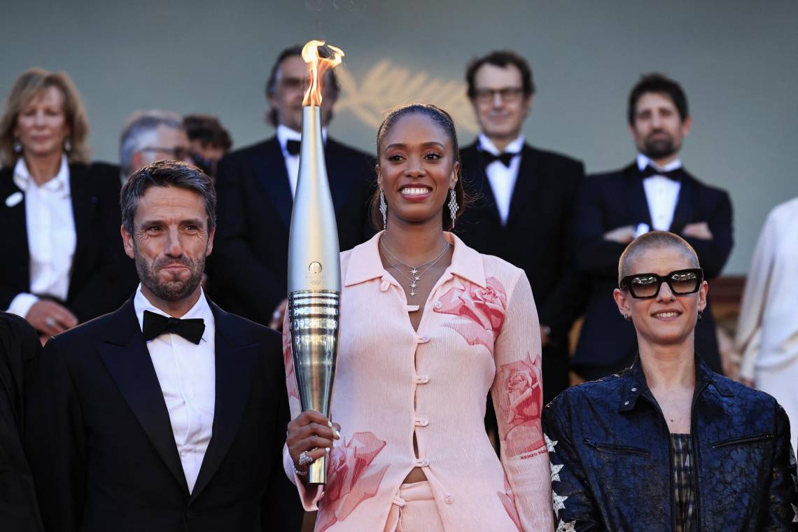 La basquetbolista francesa Iliana Rupert sostiene la antorcha olímpica junto al presidente del comité organizador de los Juegos Olímpicos y Paralímpicos París 2024, Tony Estanguet y la paraciclista francesa Marie Patouillet previo a la proyección de la película<i> Marcello Mio</i> en la 77 edición del Festival de Cannes