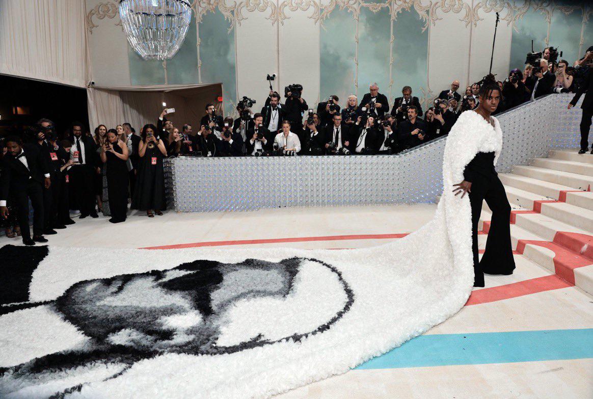 Jeremy Pope personificó uno de los legendarios momentos del desfile al llevar una capa gigante de Balmain con la cara de Karl Lagerfeld pintada a mano. Sumamente impresionante.