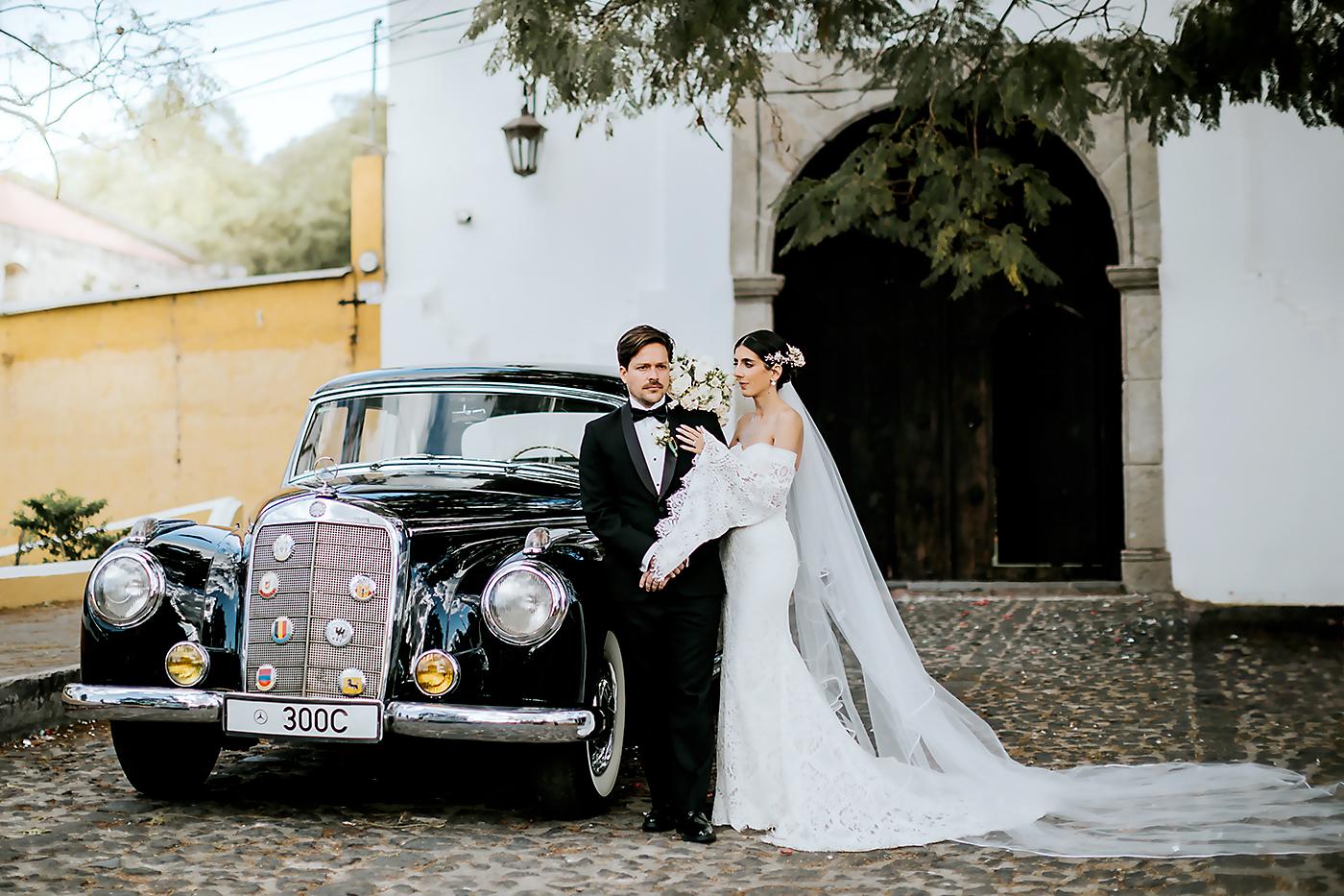 Los novios junto al coche antiguo que los llevó al lugar de la recepción en el hotel Conceptió