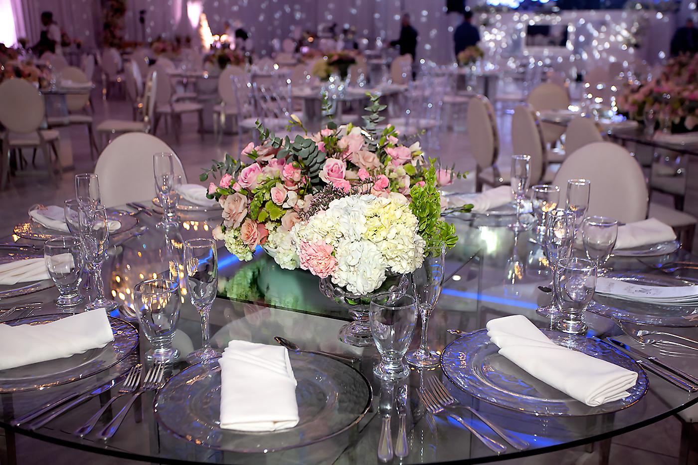 Arreglos masivos sobre bases espejadas con flores en tonos pasteles como rosados morados y verde y bastante blanco.