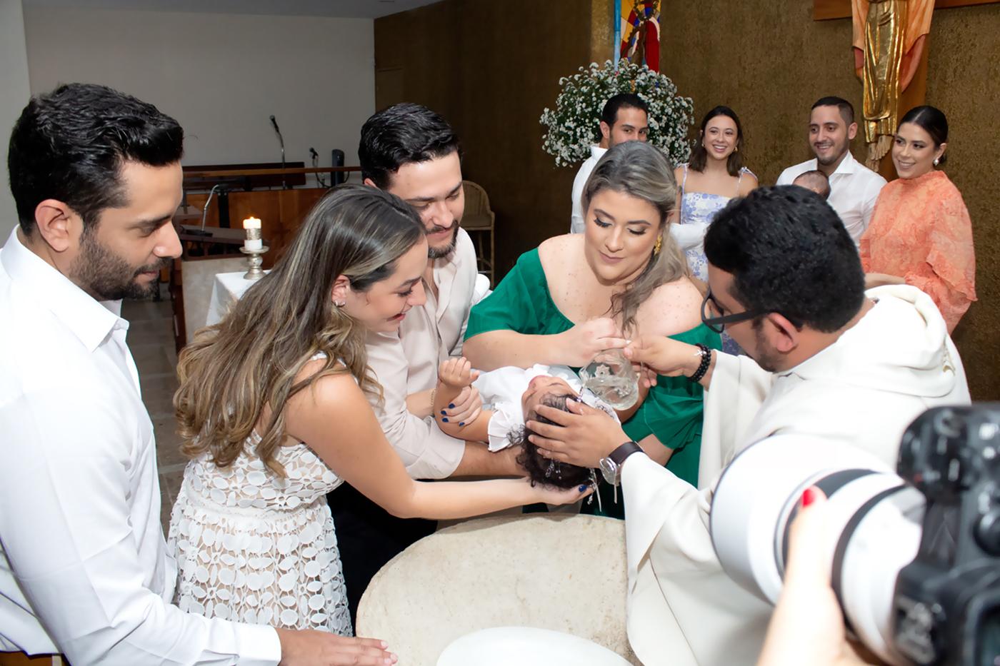 El padre Gustavo Fuentes mientras bautiza a Ana Lucía Andino rodeada de Dennys Andoni, Mari Mollieri, Juan Alberto Pineda y Alice Pineda-Andino