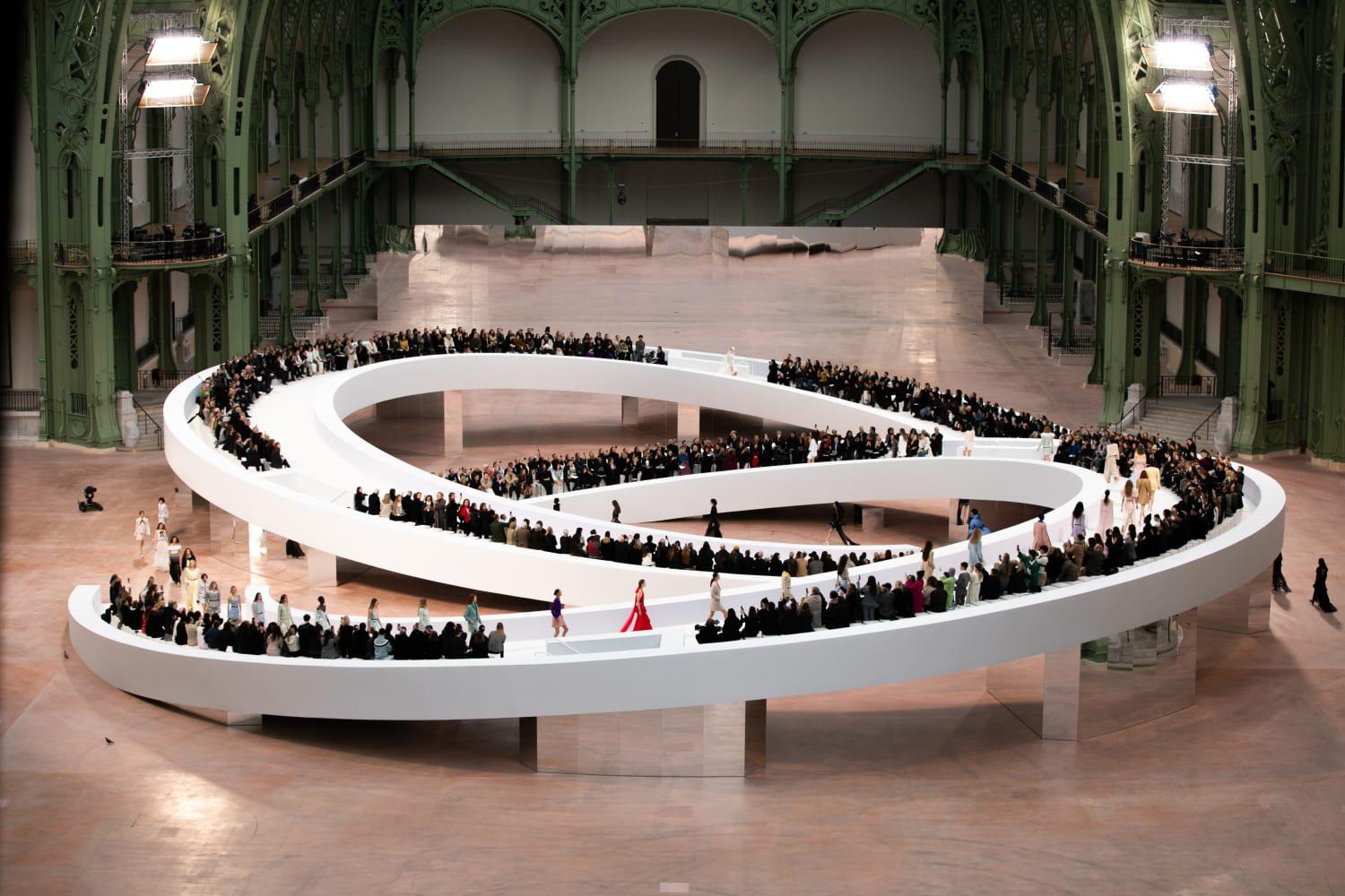 En el centro de la Nave del Grand Palais, la pista está formada por una doble C que dibuja el símbolo del infinito.La infinita excelencia de la Alta Costura, de la cual CHANEL es la Casa más antigua aún en actividad. Imaginada por el escenógrafo y diseñador Willo Perron, la estructura evoca el círculo cromático que el estudio creativo hadecidido reinterpretar. 