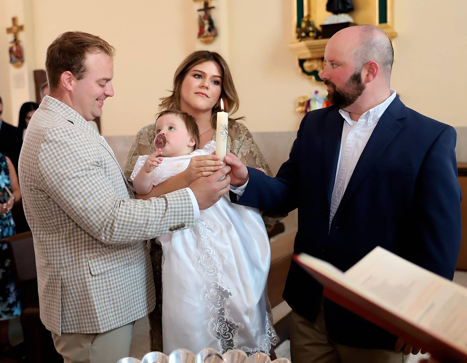 Momento en que los padrinos : María José Agüero y Álex Herzog sostienen la vela de su ahijada Bella, iluminando su camino en la fe con amor y compromiso.