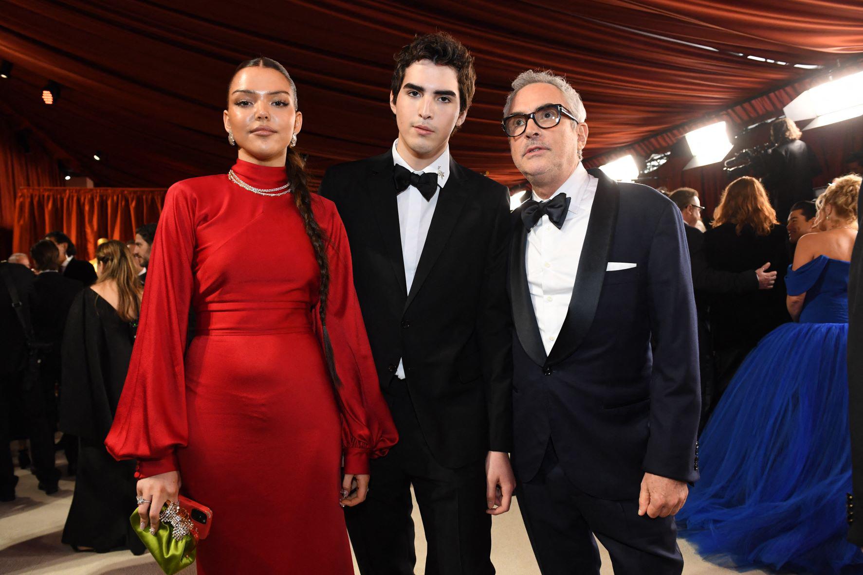 Bu Cuaron, de 19 años, llevó un vestido rojo de cuello alto y mangas obispo by Prada. En la imagen junto a su hermano Olmo y su padre, el director mexicano Alfonso Cuaron