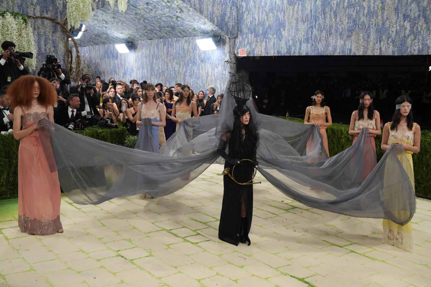 Fiel a su historia de provocar, reinterpretar y desafiar códigos, Madonna reclamó su trono. Su look partió de una base de sastrería estructurada en tonos marfil y negro, con líneas afiladas y una silueta que oscilaba entre lo ceremonial y lo teatral. Sobre esa arquitectura impecable, un capa de gran volumen y caída escultórica aportaba dramatismo sin necesidad de exageración.