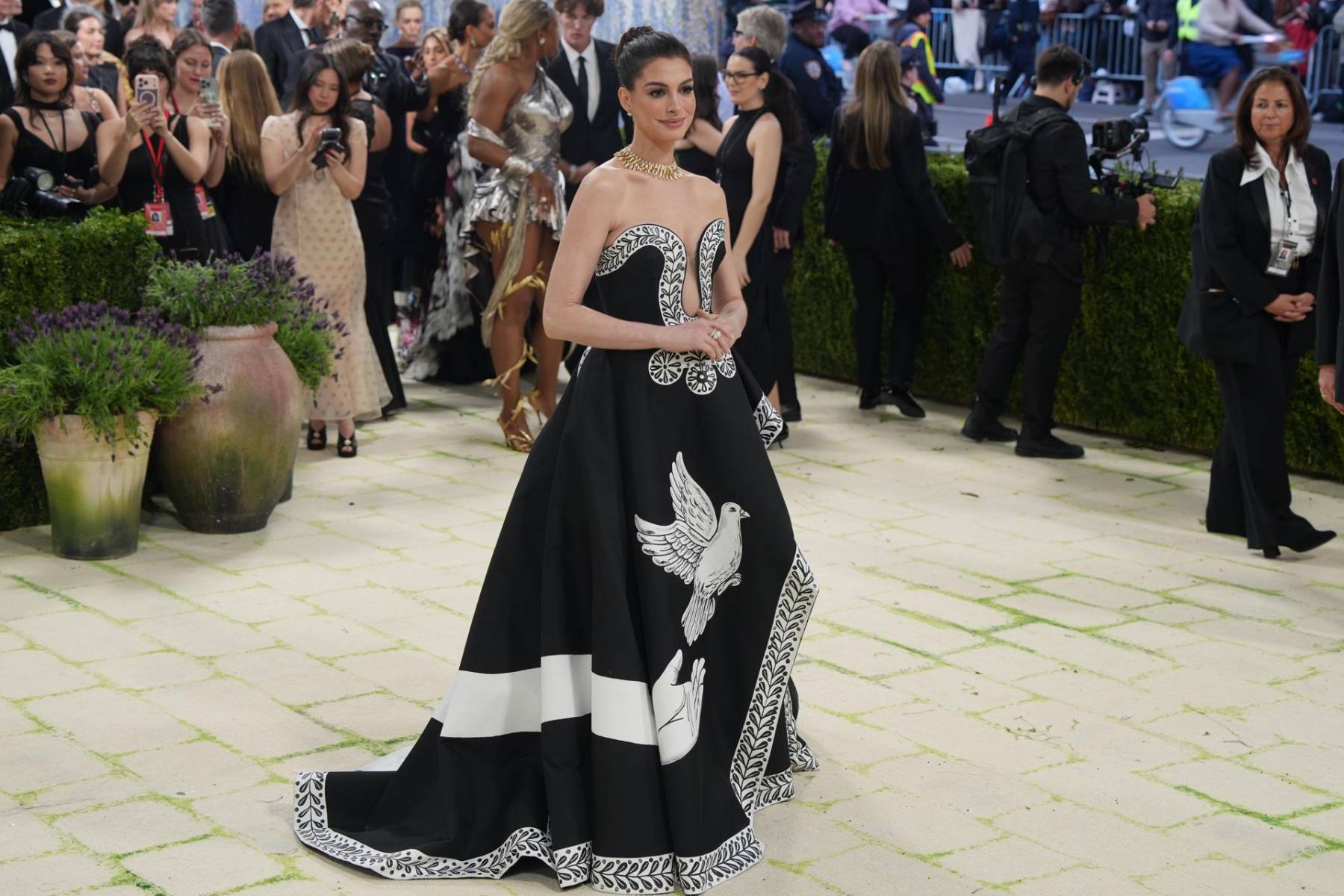 Anne Hathaway desfiló con un diseño a la medida por Michael Kors en colaboración con el artista Peter McGough, el look fue una interpretación literal —y sofisticada— del dress code. El resultado: una pieza pintada a mano confeccionada en seda mikado negra, destacó por su silueta strapless, escote pronunciado y una abertura en la pierna que aportaba dramatismo con precisión. 