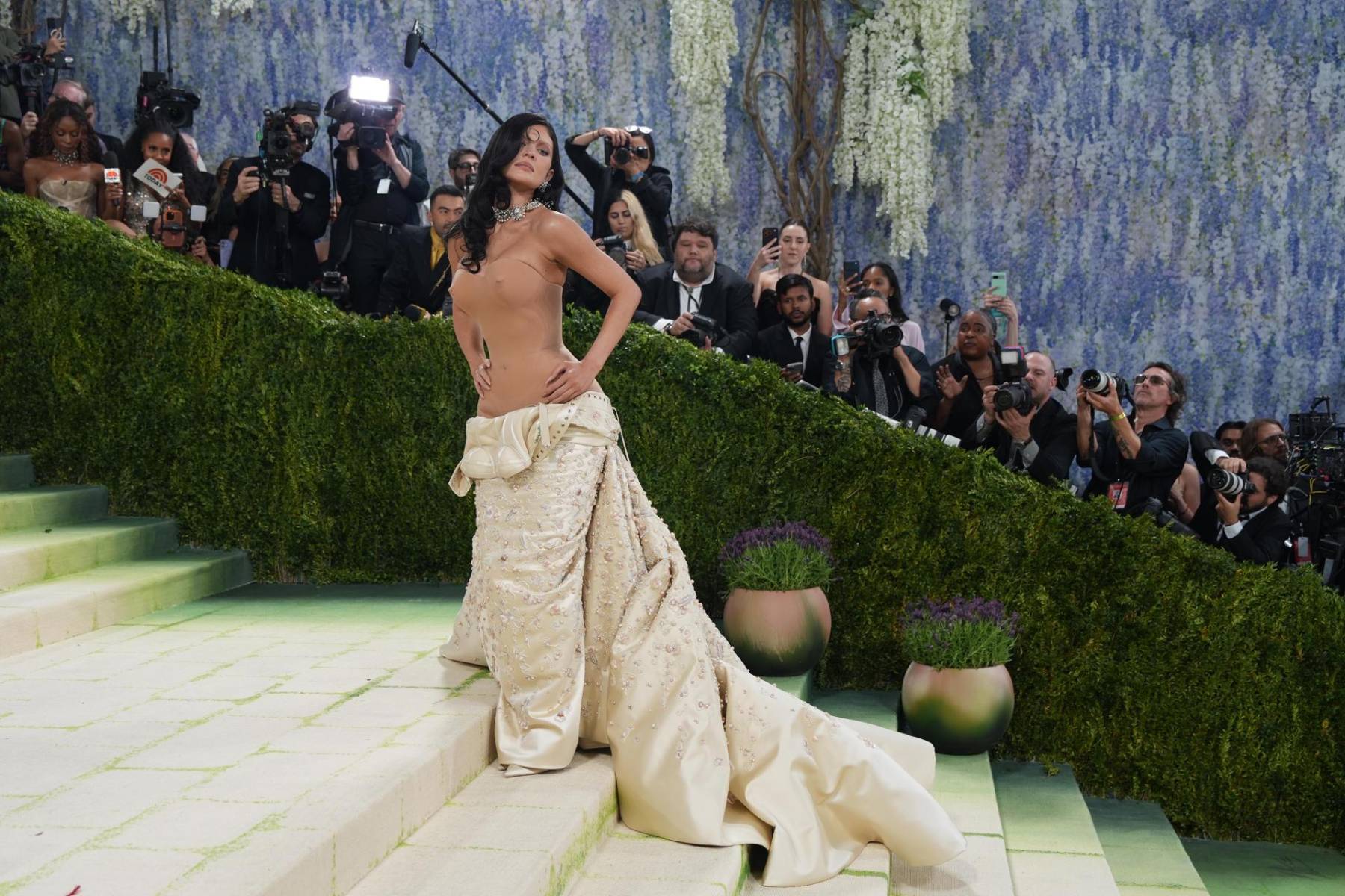 Kylie Jenner llevó un diseño de Schiaparelli, mitad escultura, mitad movimiento. El look partía de un vestido de silueta ajustada tipo corsetería, con una construcción casi escultórica que moldeaba el cuerpo como si fuera una pieza de alta joyería. 