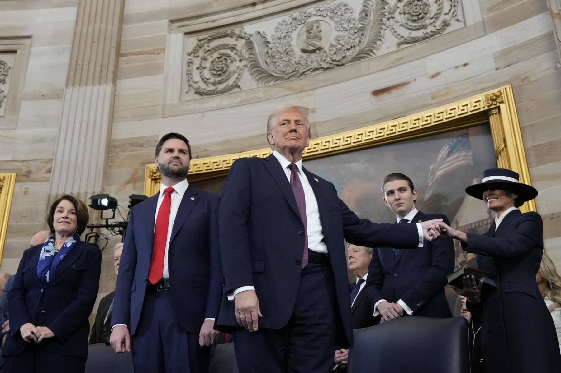 El presidente Donald Trump sostiene la mano de su esposa Melania Trump. Junto a ellos, la senadora Amy Klobuchar; el vice presidente JD Vance y Barron Trump