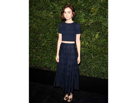 Lily Collins con un suéter negro de algodón y lino y una falda larga de algodón negro de la pre-colección Primavera-Verano Ready-to-Wear 2016, con una bolsa de la colección Otoño/Invierno Ready-to-Wear 2015/16 y sandalias CHANEL. CHANEL Fine Jewelry: aretes “Jazz” en oro blanco de 18K, diamantes y espinelas, anillo “Tuxedo” en oro blanco de 18K, diamantes y ónix, y anillo “Ultra” en oro blanco de 18K, diamantes y cerámica negra.