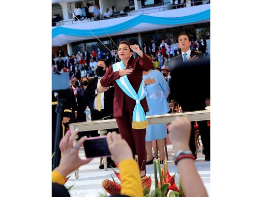 Con el Escudo Nacional en la solapa de su chaqueta y con su banda color turquesa, Xiomara Castro canta el Himno Nacional