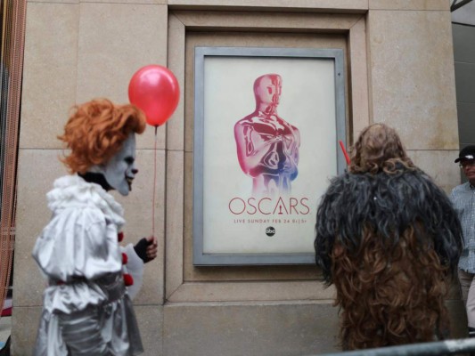 Personajes icónicos pasean en Hollywood Boulevard en frente de un cartel de los Oscars como previa a la premiación.