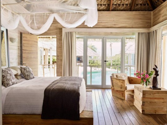 Una de las habitaciones de huéspedes revestida en madera de pino americano, con techo de palapa, amplios ventanales y cortinas de lino crudo