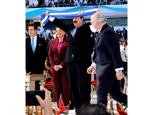 El ex mandatario Mel Zelaya sostiene la antigua banda presidencial antes de proceder a colocar a su esposa la nueva versión en turquesa