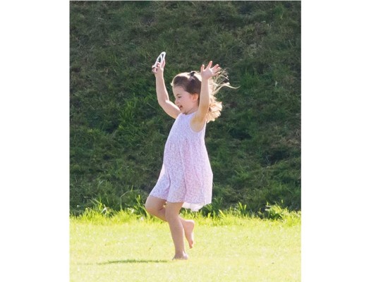 La pequeña royal llevaba puesto un vestido sin mangas en color rosa, unos lentes de sol y disfrutaba descalza de la frescura del césped