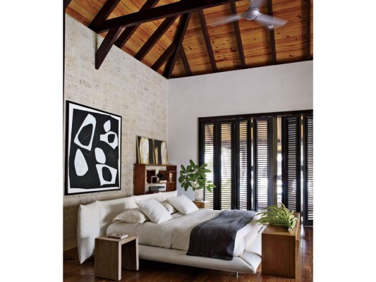 La habitación principal de la casa refleja el estilo tropical que la rodea. Una pintura XL de Fernando Varela domina la pared revestida en piedra coral. La cama es de Roche Bobois y las mesas son diseños de DM Dominicana