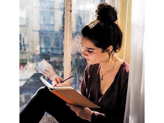 Young woman writes daily next to the window.