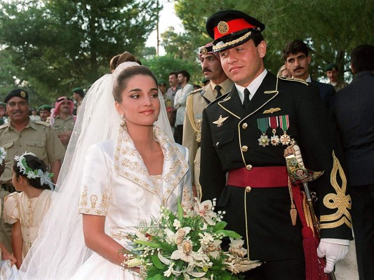 Rania de Jordania. Para su boda con el ahora rey Abdalá de Jordania en junio de 1993, la hermosa Rania de entonces 22 años llevaba un vestido de novia compuesto por una especie de chaqueta manga corta cuya solapa y mangas estaban bordadas en oro y fruncida en la cintura con una lazada, creación de Bruce Oldfield, el diseñador predilecto de Diana de Gales. El larguísimo velo que lucía iba sujeto a un moño alto. Mientras, sus manos, envueltas en guantes cortos, sostenían un bouquet de flores blancas.