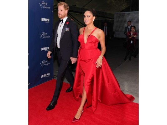 Príncipe Harry y Meghan Markle. La duquesa de Sussex escogió un vestido rojo de Carolina Herrera con tirantes y escote, mientras que el duque eligió un traje oscuro con moño y un detalle en rojo a uno de sus costados para ir a juego con su esposa.