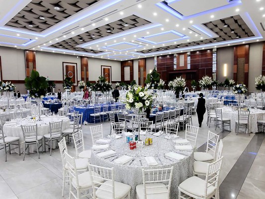 El salón lucio una decoración sobria con tonalidades en blanco, verde y azul con mesas redondas y rectangulares, adornadas con arreglos altos.