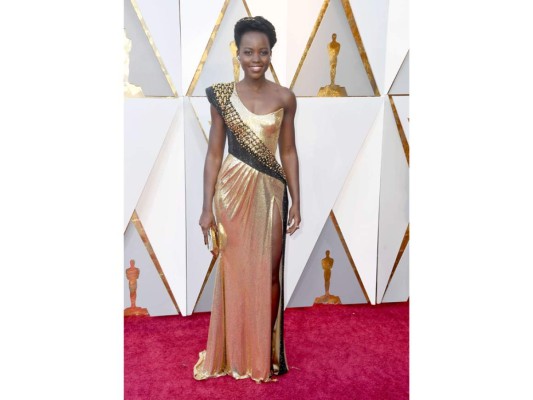Lupita Nyong'o. Apareció a la alfombra de la firma Versace. Un vestido metalizado dorado, de escote asimétrico y con un detalle negro con pedrería desde el hombro hasta la cadera. Lo complemento con una diadema dorada, pendientes en forma de flor y clutch dorado.