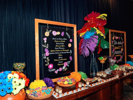 Estación de dulces adornado con hojas de mano de león pintadas y adornada con arreglos de gerberas.