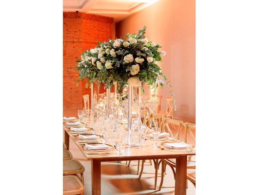 Mesas rectangulares en madera fueron decoradas con bases de cristal altas con bouquets de rosas y ramas de eucalipto