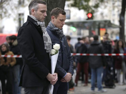 Dos hombres rinden homenaje a las víctimas de los atentados en las afueras del teatro Bataclan, uno de los sitios de los ataques terroristas en París