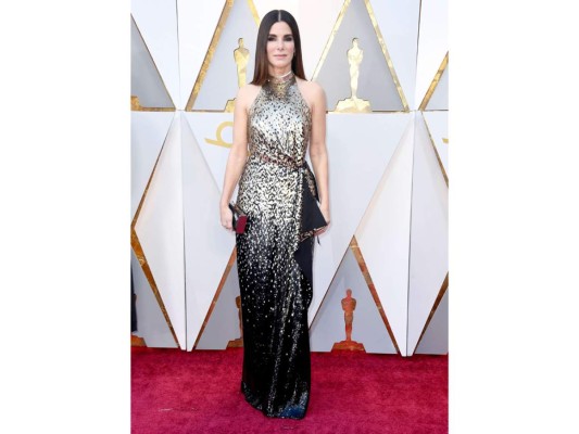 Sandra Bullock. Con un vestido dorado tornasolado con negro, de cuello halter, cintura marcada con fruncido, volante lateral, y espalda al aire, así llego la actriz quien enamoró con el diseño de Louis Vuitton que combinó con clutch caja dorado, discretos pendientes y melena ultra lisa.