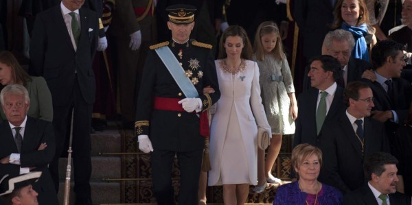 Letizia ha preferido un look en blanco roto, de vestido corto y abrigo de verano, ambos en crêpe de seda, y decorado con microperlas, amatistas, cristales de rubí y ámbar, firmado eso sí, por su modisto de confianza, Felipe Varela. Como complementos, un bolso de mano del mismo diseñador y unoz zapatos de tacón de Magrit. Y prendido de su abrigo, el lazo de la orden de Carlos III.