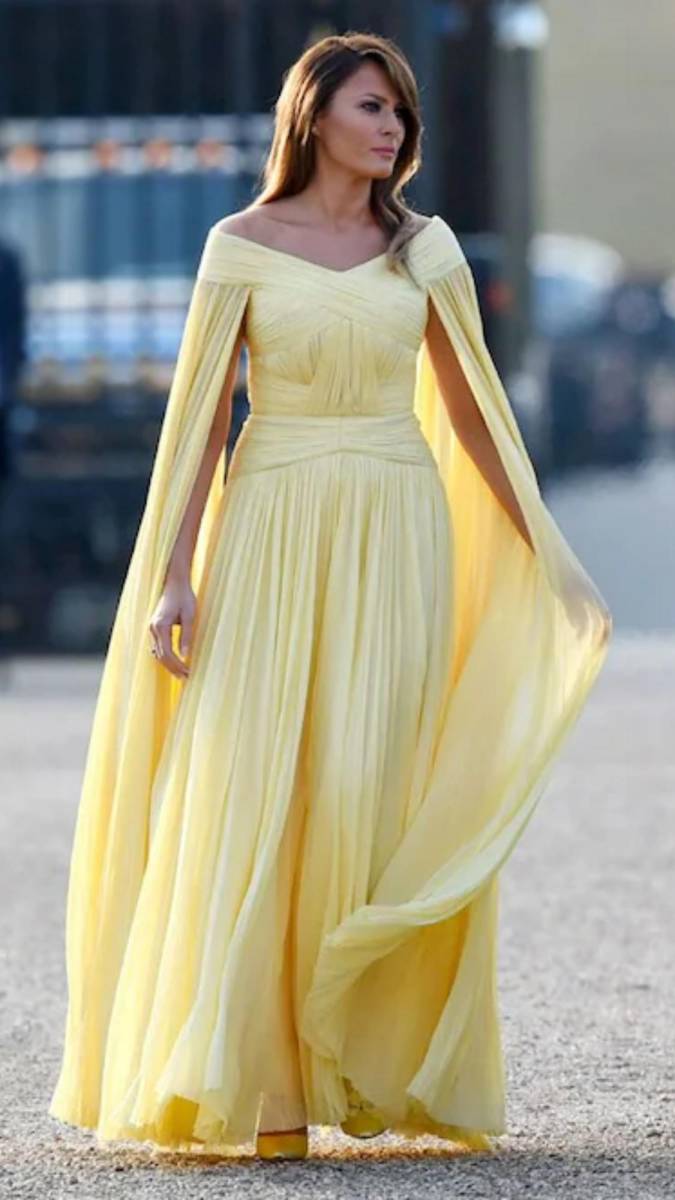 Durante la gira europea del verano de 2018, en una cena de gala en el palacio de Blenheim en Inglaterra, Melania Trump eligió un vestido plisado de delicado tono amarillo con capa, diseñado por <b>J. Mendel</b>. Este look evocó de inmediato comparaciones con Bella, la princesa de Disney, y se destacó como uno de sus momentos más memorables en estilo, transmitiendo un aire de elegancia digna de cuento.