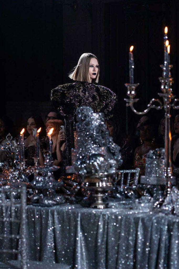 Candelabros de plata con velas encendidas iluminaban bandejas de pan, canastas de frutas y pasteles de varios niveles, todo cubierto con brillo plateado y colocado sobre manteles plateados. Este escenario mágico durante el desfile de Rodarte.