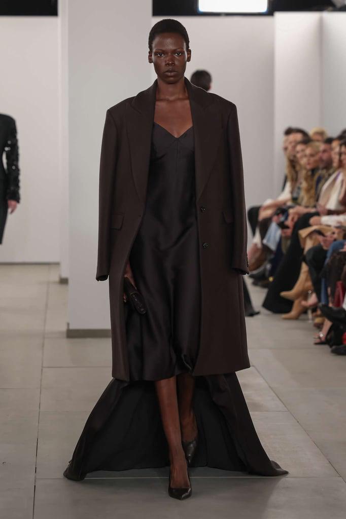 Chaqueta negra cruzada alargada sobre un vestido lencero de seda negro hasta la rodilla con una cola dividida inspirado en el vestido de novia de su abuela.