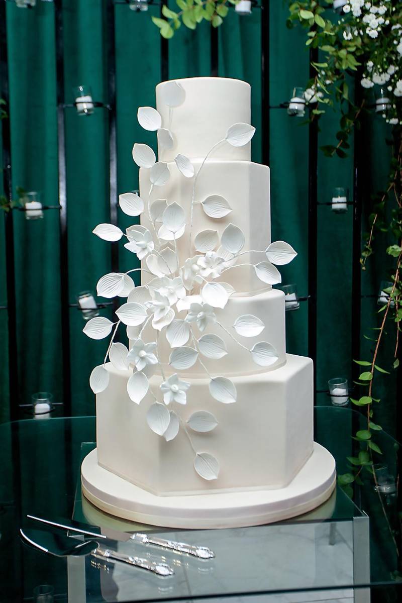 Pastel de boda de 4 niveles con diseño moderno de cascadas irregulares de hojas y flores elaboradas a mano en fondant con sabor a brandy, pralines y amaretto de Signature Cake.