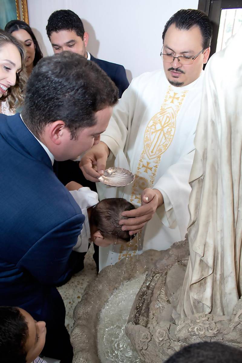 Jorge Alvarenga, sostiene a su ahijado Daniel Emilio, mientras el padre José Luis López deja caer el agua sobre el nuevo cristiano.