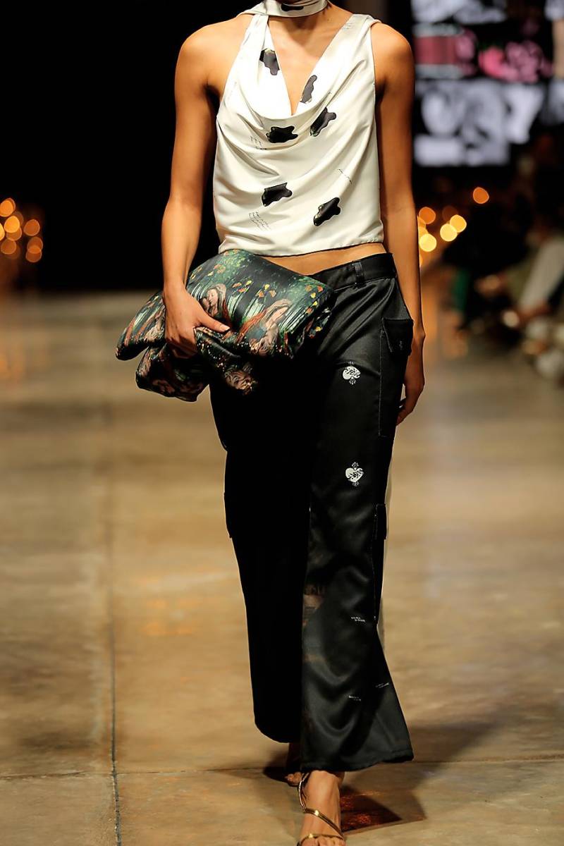  Un top drapeado con corte asimétrico se combina con un pantalón negro. El clutch acolchado, con el estampado con motivo religioso, que predomina a través de la colección, añade un toque artístico.