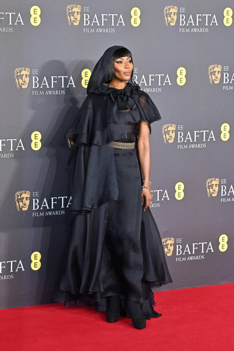 Naomi Campbell, la supermodelo apostó por un vestido tobillero de Chanel negro con cinturón que completó con una capa con capucha de gasa con volantes que caían a distintos niveles: hombros, caderas y pantorrillas. 
