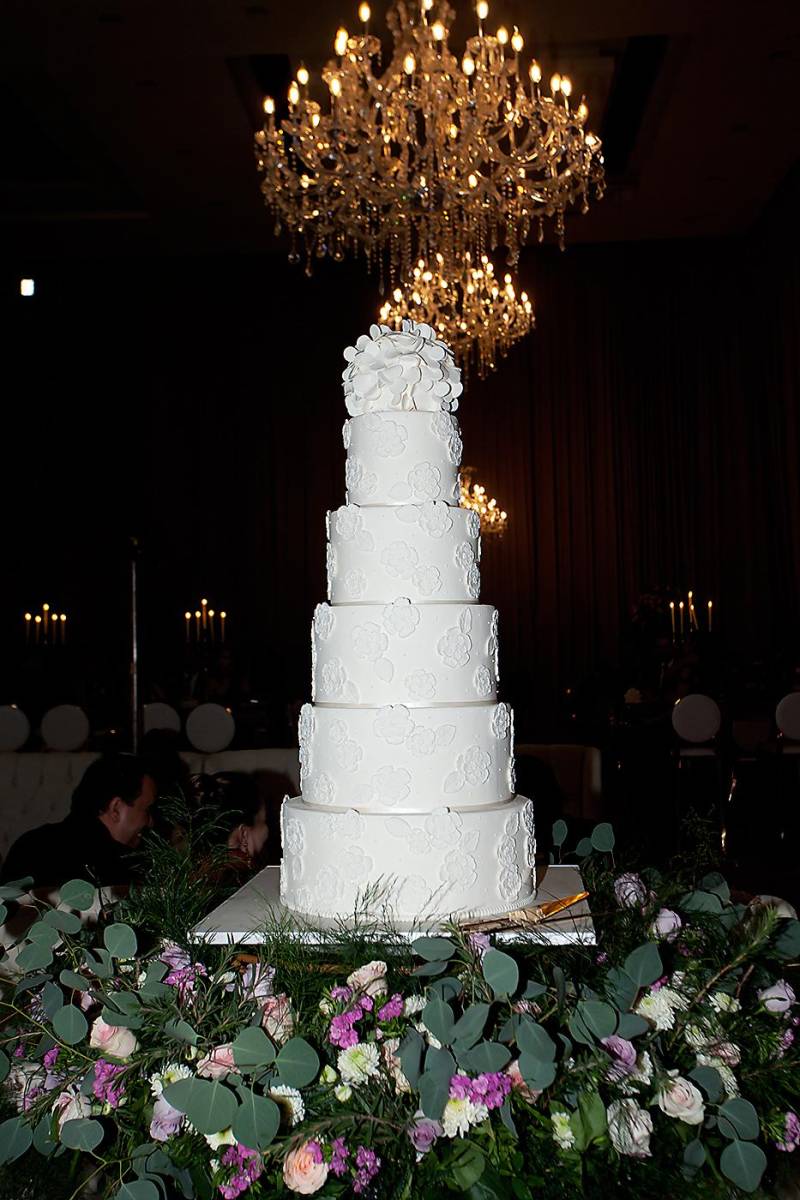 Pastel de 5 niveles con encaje francés elaborado en azúcar con bouquet de pétalos blancos. Torta de biscotti relleno de frambuesa, elaborado por los expertos de Signature Cake