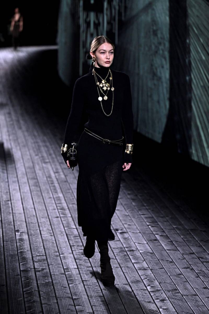 La supermodelo Gigi Hadid desfiló con un discreto conjunto de falda y suéter negro, lazo Chanel en el cabello y una hábil cascada de collares estilo años 20 en oro 
