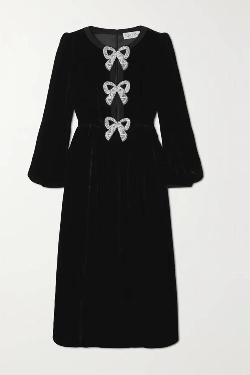 Inspirado en estilos vintage, el glamuroso vestido tiene un atractivo escote dividido unido por tres lazos decorativos, cada uno densamente adornado con perlas artificiales, cuentas iridiscentes y cristales brillantes. 