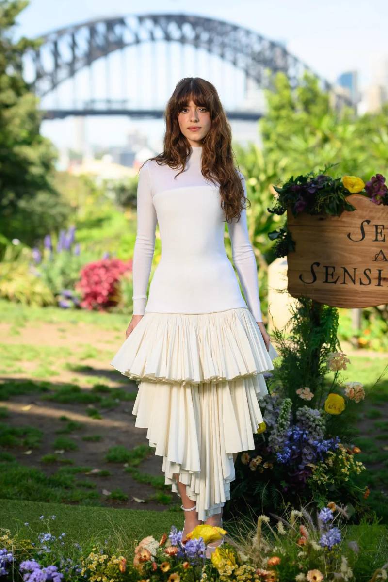 Siempre en la isla de Australia, la protagonista de <i>Sense and Sensibility</i> lució etérea en el Wendy’s Secret Garden con un top manga larga de cuello alto de silueta tipo hourglass, y una falda de volantes escalonados en tonalidad crema, vistiendo Alaïa de pies a cabeza.