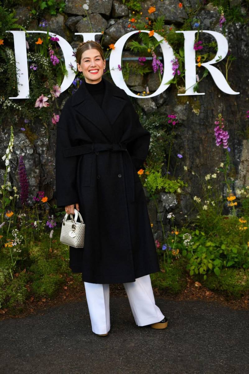 Rosamund Pike lució un trench coat negro sobre un turtleneck del mismo color y optó por utilizar su cabello en un elegante peinado recogido.