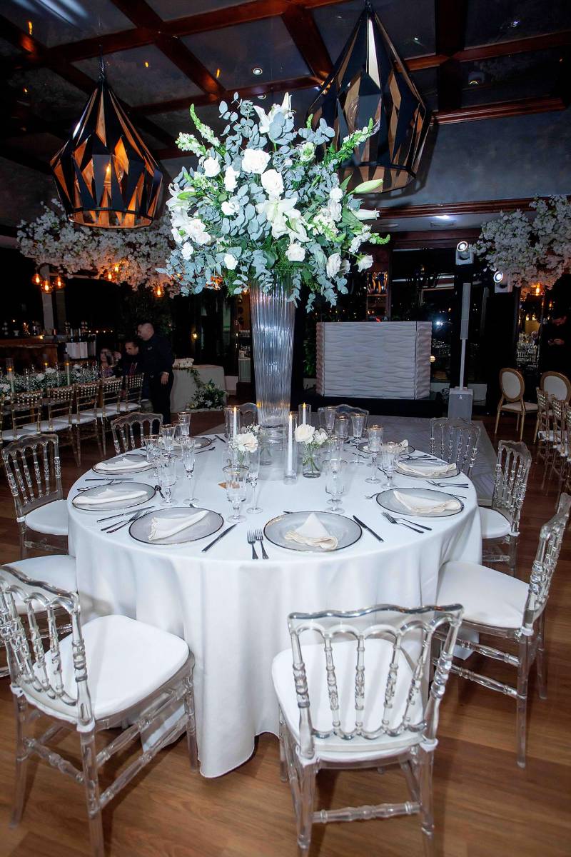 Mesas circulares con ghost chair y bases de vidrio alto con velas y ramas de eucalipto, rosas y baby breath.