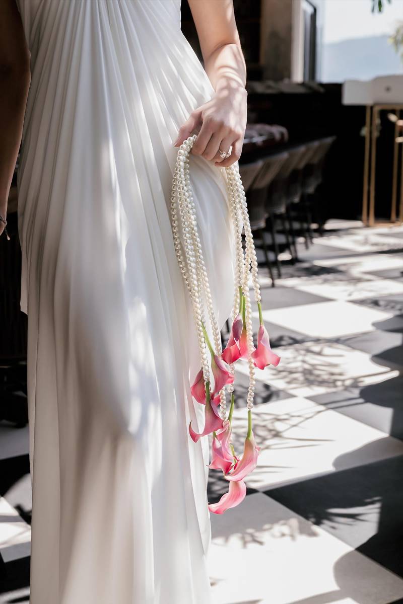 El bouquet añade un toque artístico: flores de calla rosadas con largas hebras de perlas en cascada, creando un efecto elegante y moderno.